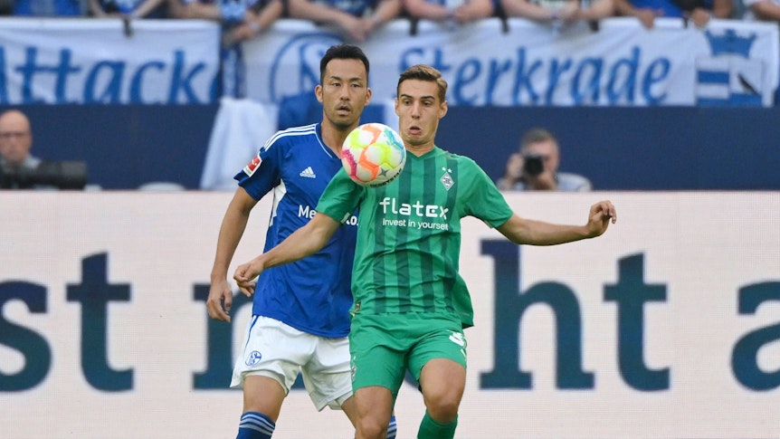 Florian Neuhaus (r.) von Borussia Mönchengladbach steht beim Bundesliga-Auswärtsspiel bei Schalke 04 am 13. August 2022 vor Maya Yoshida und blickt fokussiert auf den Ball vor ihm.