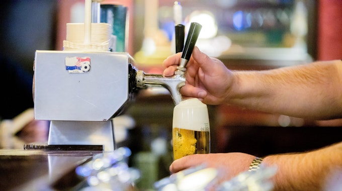 Ein Kneipenwirt zapft in einer Gaststätte Bier.
