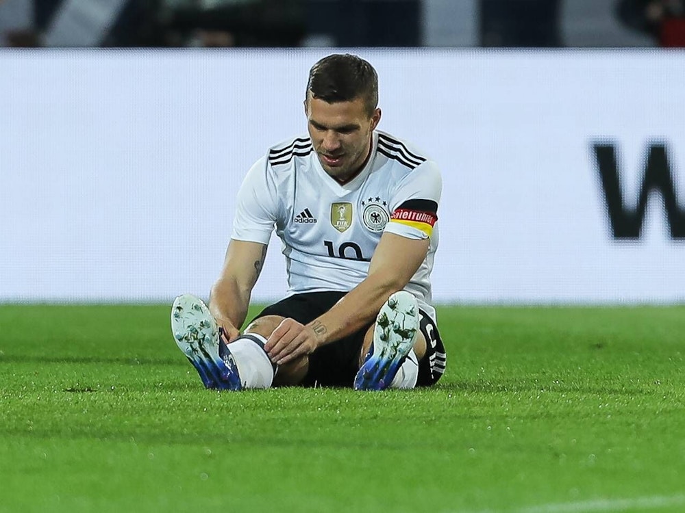 Lukas Podolski sitzt auf dem Rasen und richtet seinen rechten Stutzen.