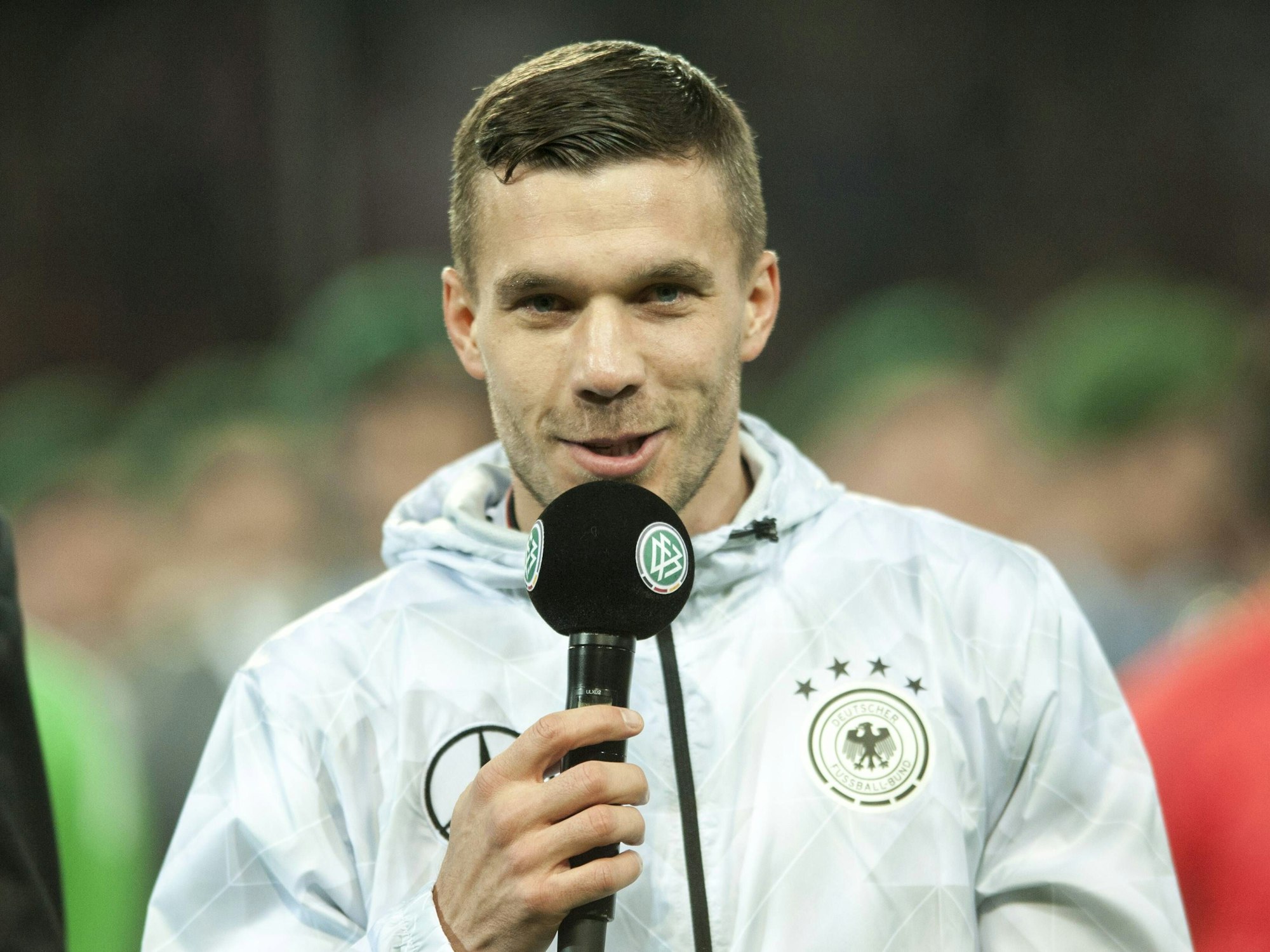 Lukas Podolski mit einem Mikrofon in der Hand.