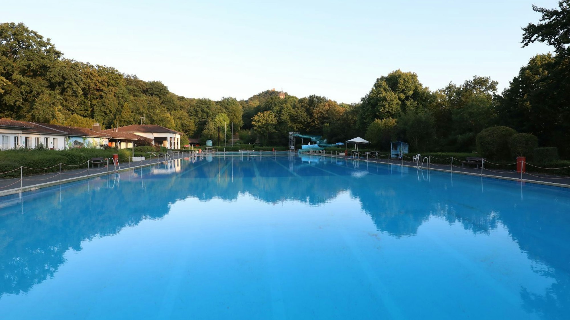 Ein großes Schwimmbecken mit blauem Wasser, im Hintergrund stehen Bäume.