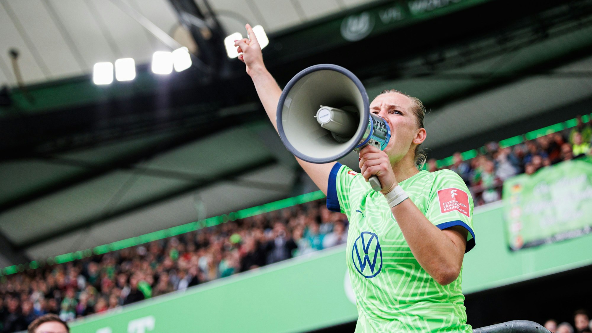 Alexandra Popp vom VfL Wolfsburg steht auf dem Zaun und feiert mit Wolfsburger Fans nach Spielende und spricht durch ein Megaphon der Fans. 