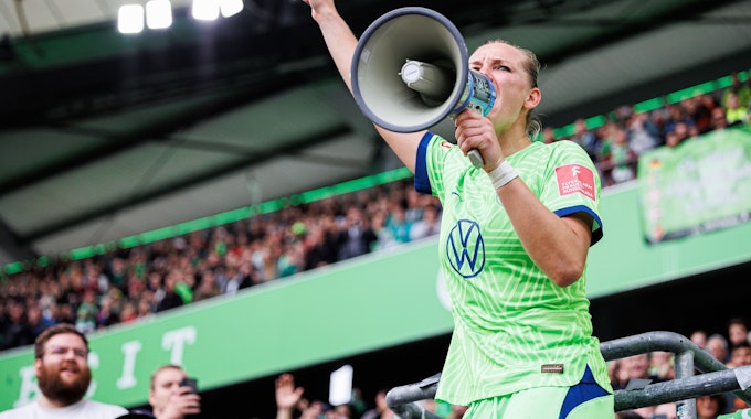 Alexandra Popp vom VfL Wolfsburg steht auf dem Zaun und feiert mit Wolfsburger Fans nach Spielende und spricht durch ein Megaphon der Fans. 