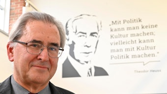 Klaus Füßmann steht vor einem Zitat von Theodor Heuss an einer Wand. Das Zitat lautet: „Mit Politik kann man keine Kultur machen, vielleicht kann man mit Kultur Politik machen.“