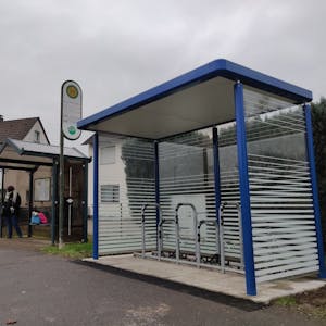 An der Bushaltestelle in Büscherhöfen steht neben dem Wartehäuschen für Busfahrgäste ein neuer blauer verglaster Unterstand mit Schlossbügeln für Radfahrer.