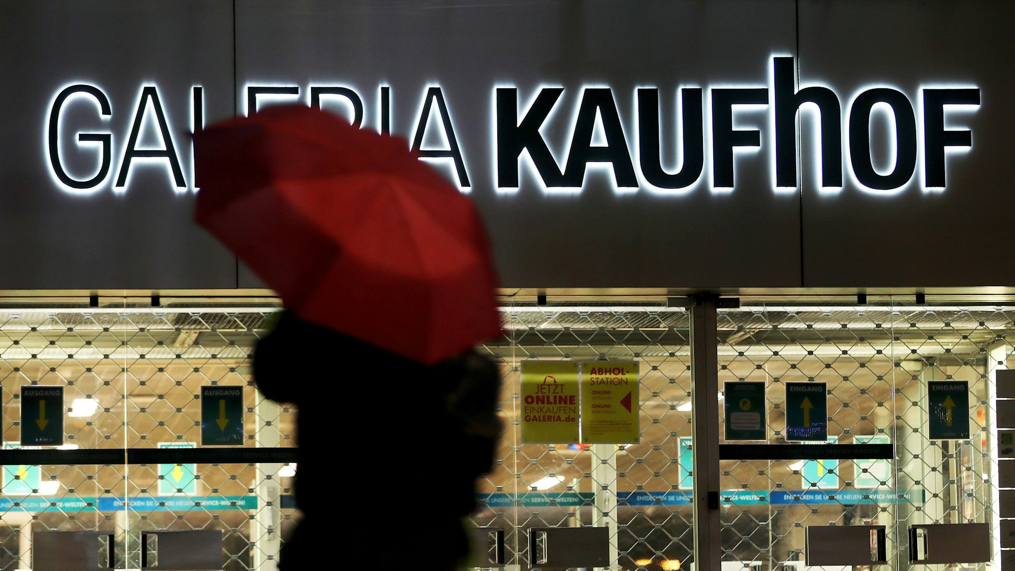 ARCHIV - 27.01.2021, Nordrhein-Westfalen, Köln: Eine Frau geht mit Regenschirm an einer geschlossenen Kaufhof Filiale vorbei.