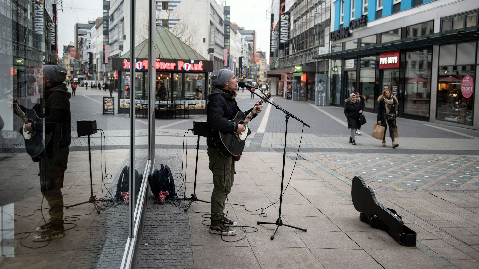Ein Straßenmusiker  spielt in der Fußgängerzone auf seiner Gitarre und singt.
