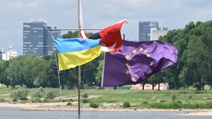 Eine ukrainische Fahne weht neben einer EU-Fahne im Wind, im Hintergrund der Rhein.&nbsp;