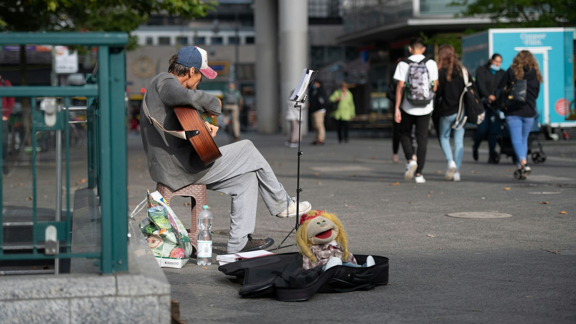 Ein Straßenmusiker sitzt mit Gitarre in einer Fußgängerzone.