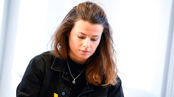 Die deutsche Klimaschutzaktivistin Luisa Neubauer vor einem Fenster. Auf ihrer schwarzen Jacke trägt sie ein gelbes X, um sich mit dem Widerstand gegen den Abriss des Braunkohledorfs Lützerath zu solidarisieren.