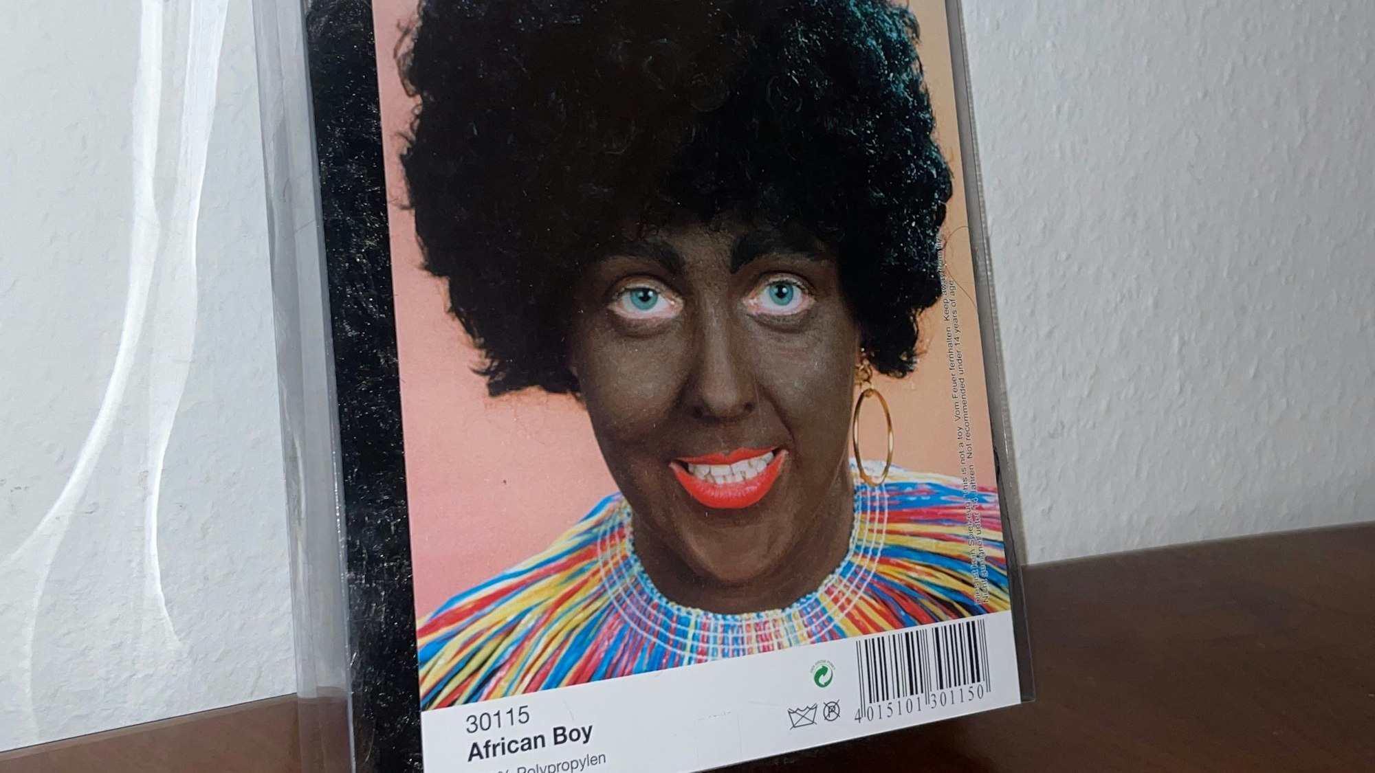 Eine Karnevalsperücke eines Kölner Kostümhändlers steht in der Kritik. Der Produktname „African Boy“ und die Beschminkung der Person haben eine rassistische Geschichte und bringen deshalb Empörung hervor.