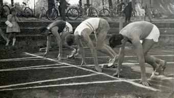Athleten an der Startlinie auf einer Laufbahn. Das Bild ist in schwarz-weiß.