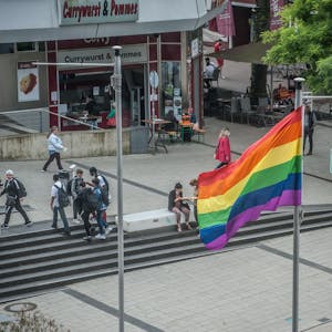 Im Juni 2021 weht auf dem Rathausvorplatz in Wiesdorf eine Regenbogenfahne. Passanten flanieren, Schüler stehen beieinander.