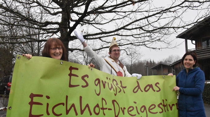 Drei Menschen haben ein grünes Banner in der Hand auf dem steht: „Es grüßt das Eichhof-Dreigestirn“.
