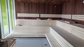 Blick in die Sauna mit weißen Holzbänke und dunkel vertäfelten Holzwänden.