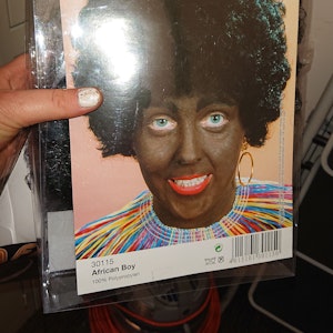 Eine schwarze Perücke als Karnevalskostüm mit der Verpackungsaufschrift African Boy.