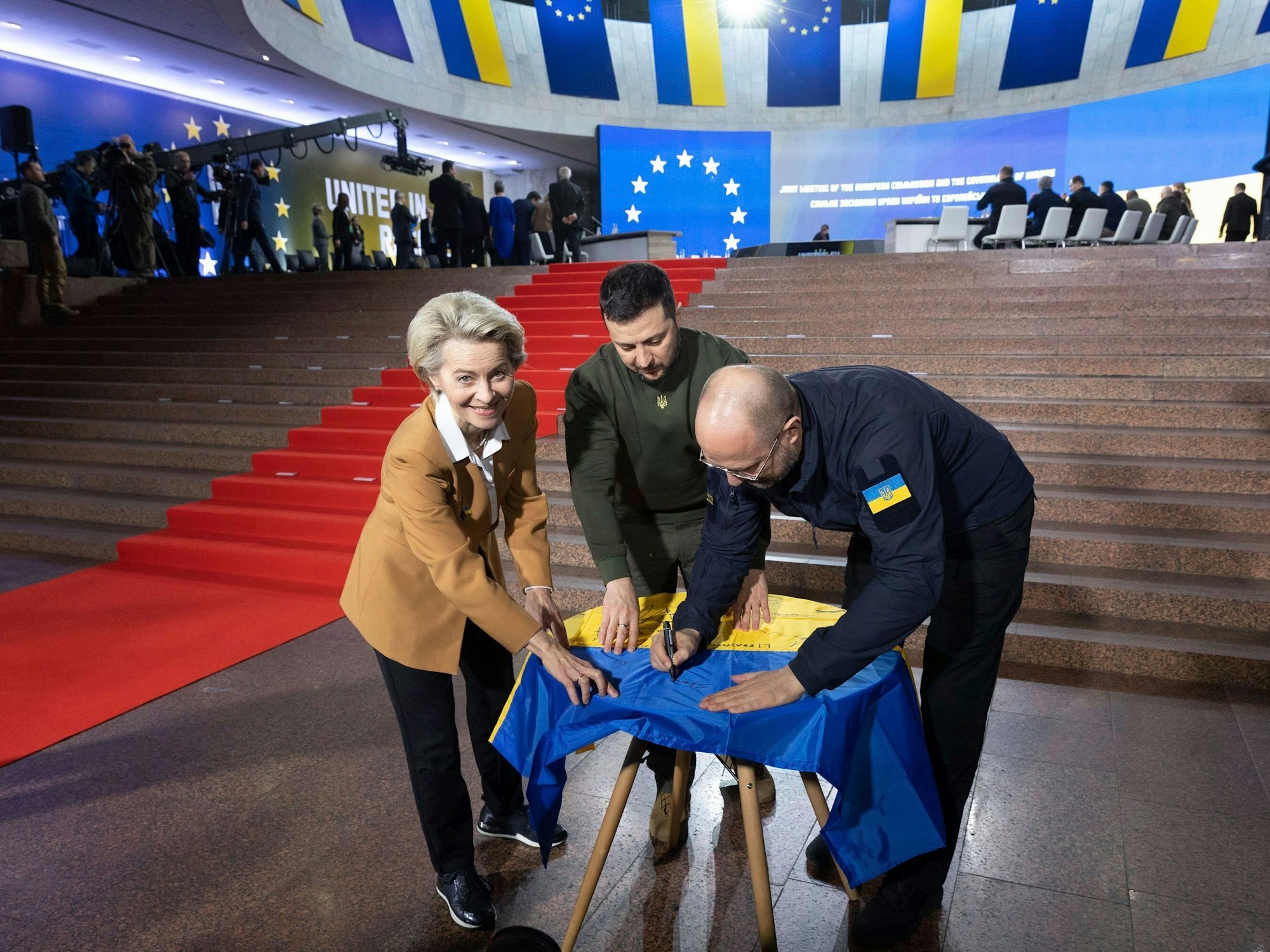 Wolodymyr Selenskyj (M), Präsident der Ukraine, und Ursula von der Leyen, und Denys Schmyhal, Ministerpräsident der Ukraine, schreiben ihre Wünsche auf eine ukrainische Fahne während des EU-Ukraine-Gipfels. Erstmals seit der Beginn der russischen Invasion in die Ukraine reisen gleich 16 Vertreter der EU-Kommission in die Hauptstadt Kyjiw. Die Reise ist vor allem ein Zeichen dafür, dass die EU weiter an der Seite des angegriffenen Landes steht. +++ dpa-Bildfunk +++