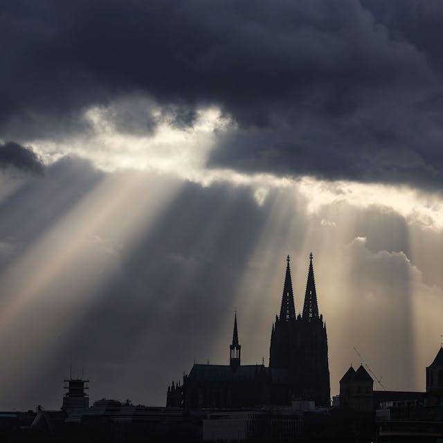 Köln: Sonnenstrahlen scheinen hinter dem Dom aus Wolken.
