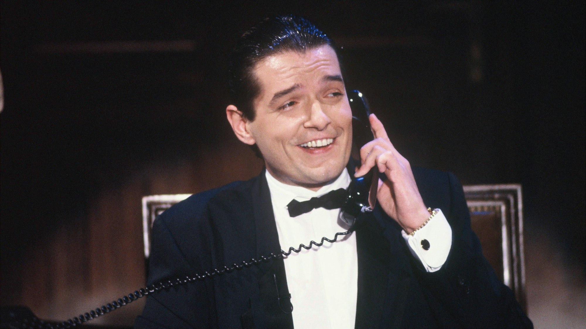 Der Sänger Falco bei einem TV-Auftritt in der Show „Wir gratulieren“ am 6.10.1985. Falco hält einen Telefonhörer und lacht.