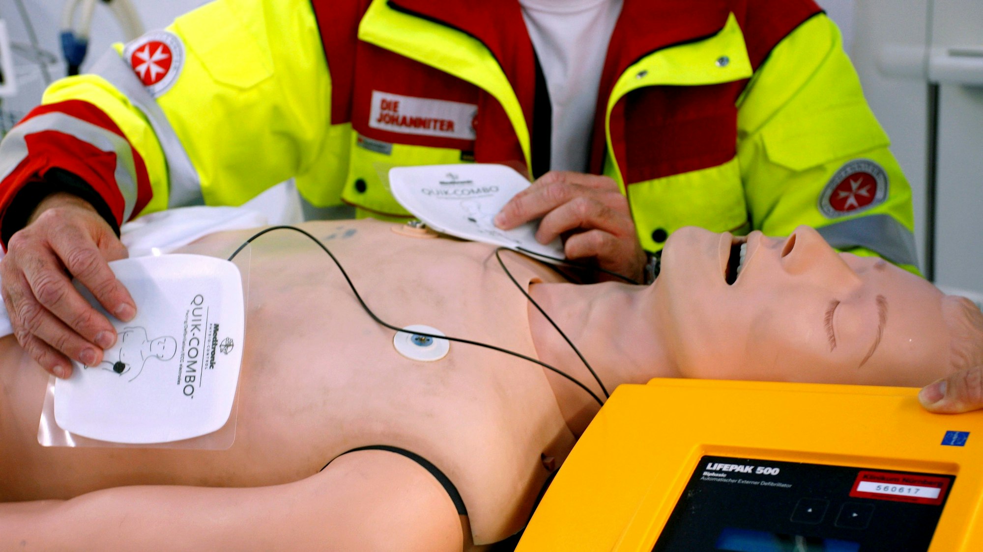 Ein Rettungssanitäter präsentiert einen Defibrillator an einer Puppe.