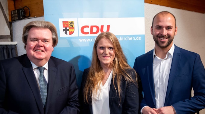 Zwei Männer und eine Frau stehen vor einem CDU-Plakat.