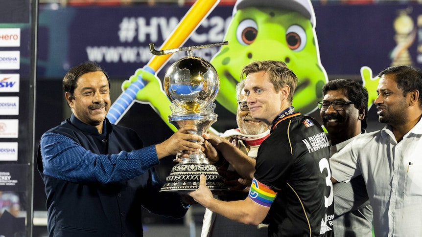 So sehen Weltmeister aus! Deutschland-Kapitän und Fohlen-Fan Mats Grambusch (r.) bekommt die Hockey-Trophäe am 29. Januar 2023 in Indien überreicht. Grambusch lächelt, er trägt eine Regenbogen-Armbinde.