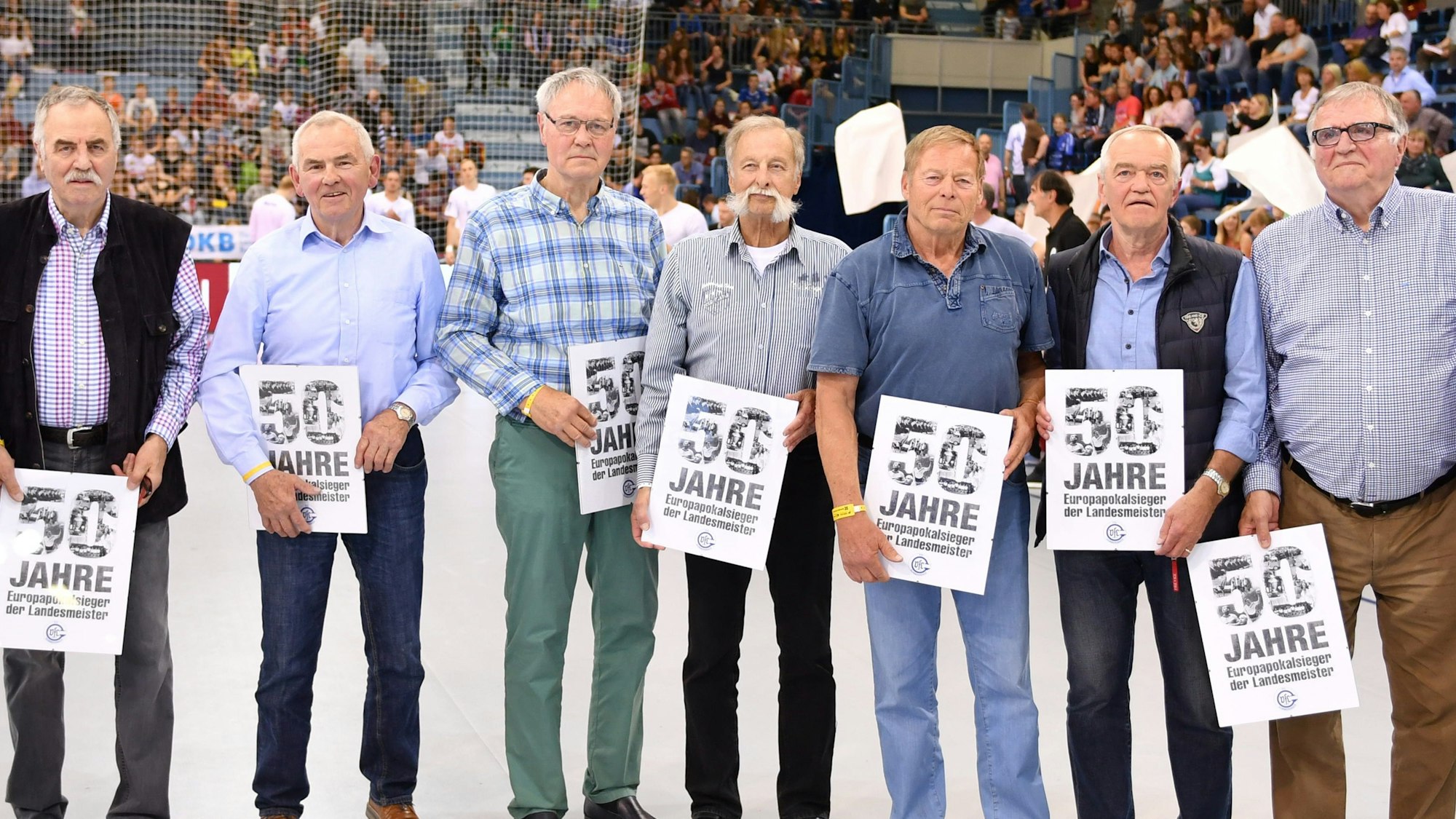 Mehrere Männer des VfL Gummersbach stehen nebeneinander. In den Händen halten sie die Chronik zum 50-jährigen Bestehen des VfL Gummersbach.