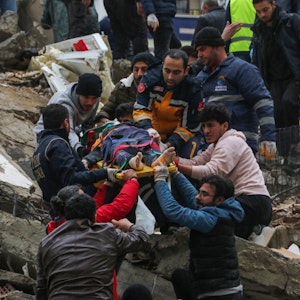 Nach dem verheerenden Erdbeben in der Nacht vom 5. auf den 6. Februar 2023 bergen Rettungskräfte und weitere Helfer auf einer Bahre einen Menschen aus einem eingestürzten Gebäude in Adana (Türkei).