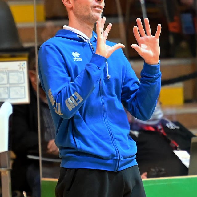 Ein Volleyballtrainer gestikuliert am Spielfeldrand.