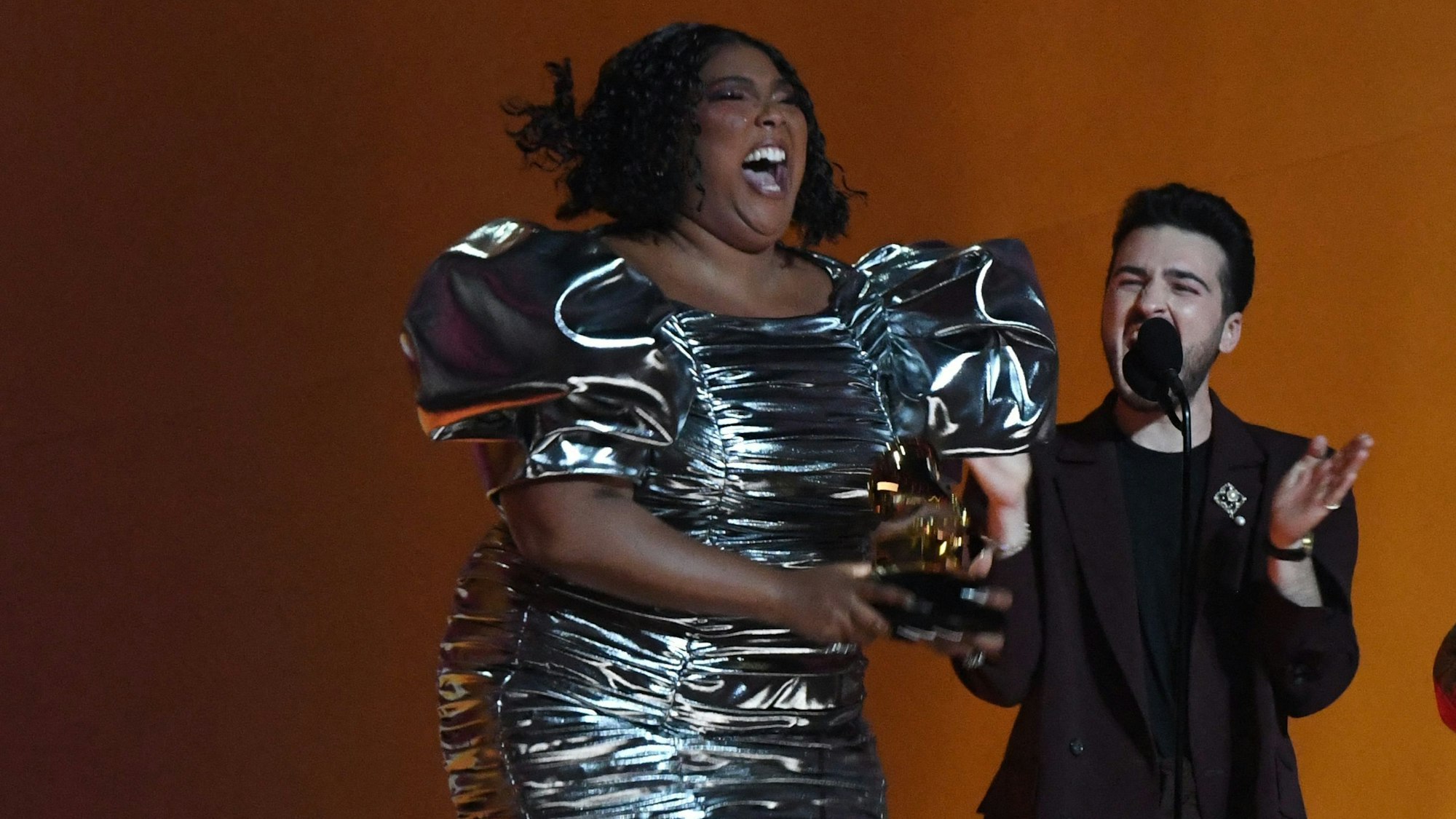 Lizzo hüpft im kurzen silbernen Kleid auf der Bühne der Grammy Awards in Los Angeles. In ihren Händen hält sie den Preis für die beste Aufnahme des Jahres.