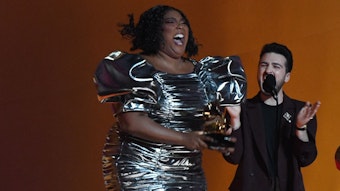 Lizzo hüpft im kurzen silbernen Kleid auf der Bühne der Grammy Awards in Los Angeles. In ihren Händen hält sie den Preis für die beste Aufnahme des Jahres.