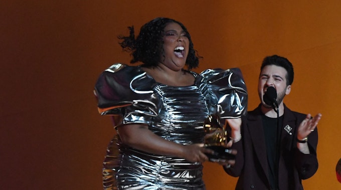 Lizzo hüpft im kurzen silbernen Kleid auf der Bühne der Grammy Awards in Los Angeles. In ihren Händen hält sie den Preis für die beste Aufnahme des Jahres.&nbsp;