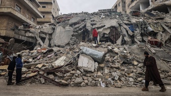 Menschen betrachten die Trümmer eines zerstörten Wohnhauses.