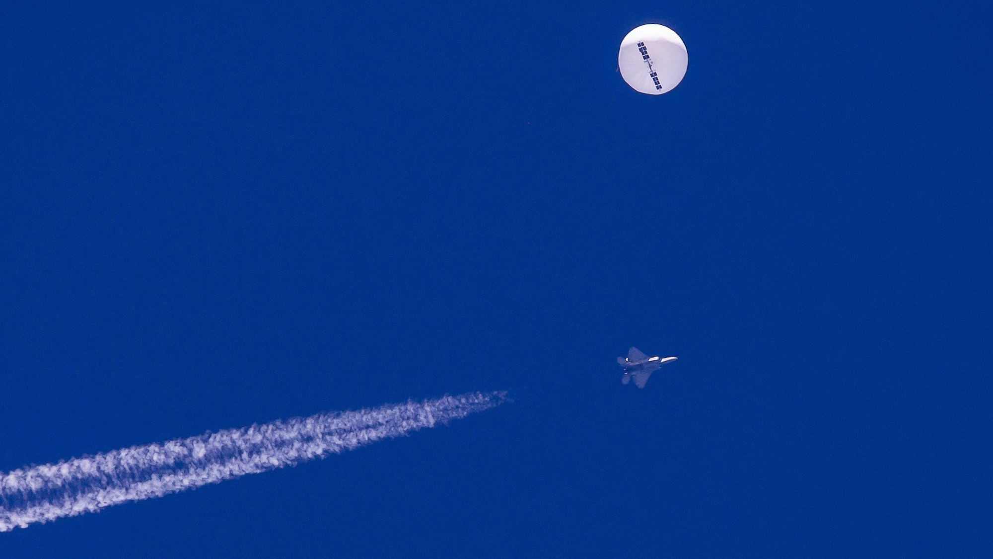 Ein großer Ballon schwebt über dem Atlantischen Ozean vor der Küste von South Carolina. Darunter sind ein Kampfjet und seine Kondensstreifen zu sehen.