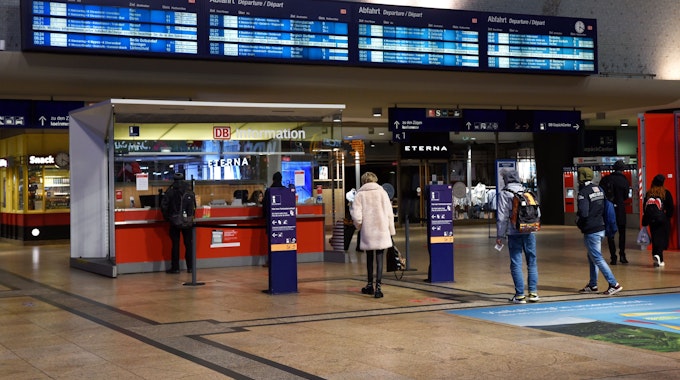 Menschen stehen vor dem Service-Point am Haupteingang des Kölner Hauptbahnhofs und warten.