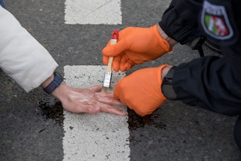 Ein Polizist entfernt mit Speiseöl und Pinsel die auf dem Asphalt festgeklebte Hand einer Aktivistin.