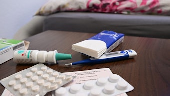Ein Fieberthermometer, Medikamente und eine ärztliche Arbeitsunfähigkeitsbescheinigung (Krankmeldung) liegen auf einem Nachttisch