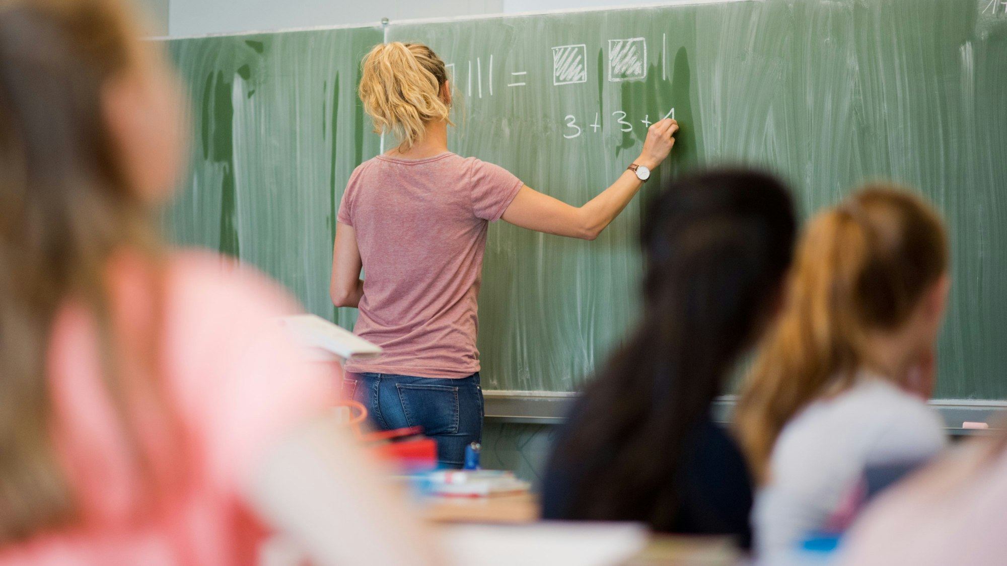 Eine junge Lehrerin schreibt an eine Schultafel im Mathematikunterricht an einer Integrierten Gesamtschule.