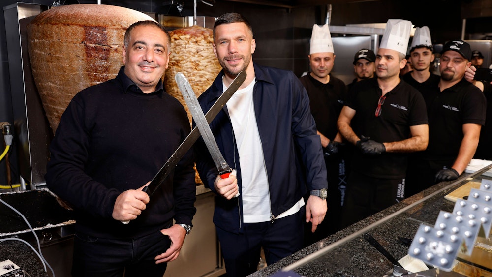 Geschäftsführer Metin Dag und Fußballer Lukas Podolski stehen hinter der Theke bei Mangal-Döner.