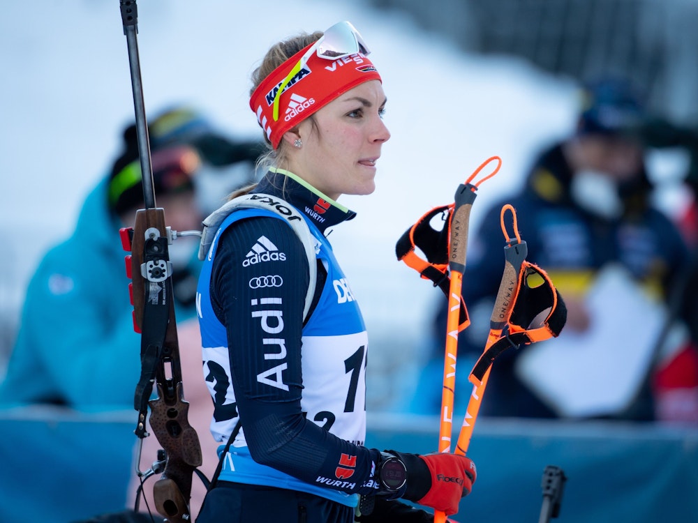 Biathletin Hanna Kebinger aus Deutschland bereitet sich auf ein Rennen vor. In der rechten Hand trägt sie ihre Skistöcke, auf dem Rücken ihr Gewehr.