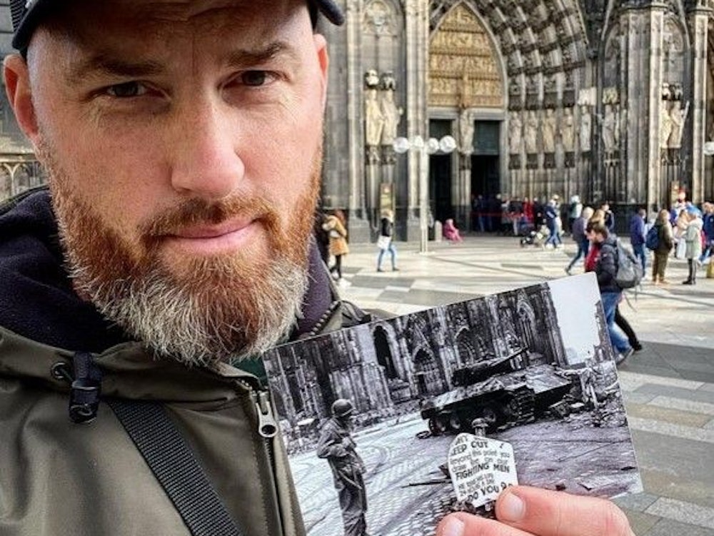 Ein Mann hält ein Foto vor dem Kölner Dom in der Hand.