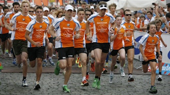In orange und schwarz gekleidete Läufer sprinten über den Kölner Heumarkt.