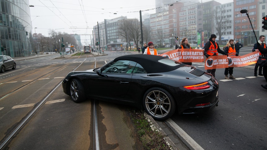 Ein Porsche umfährt die Straßensperre der Letzten Generation und fährt über die Gleise.