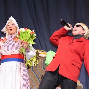 Zwei Frauen stehen auf der Bühne. Eine verkleidet als Frau Antje, mit bunten Tulpen in der Hand, die andere als Heino, der in ein Mikrofon singt.