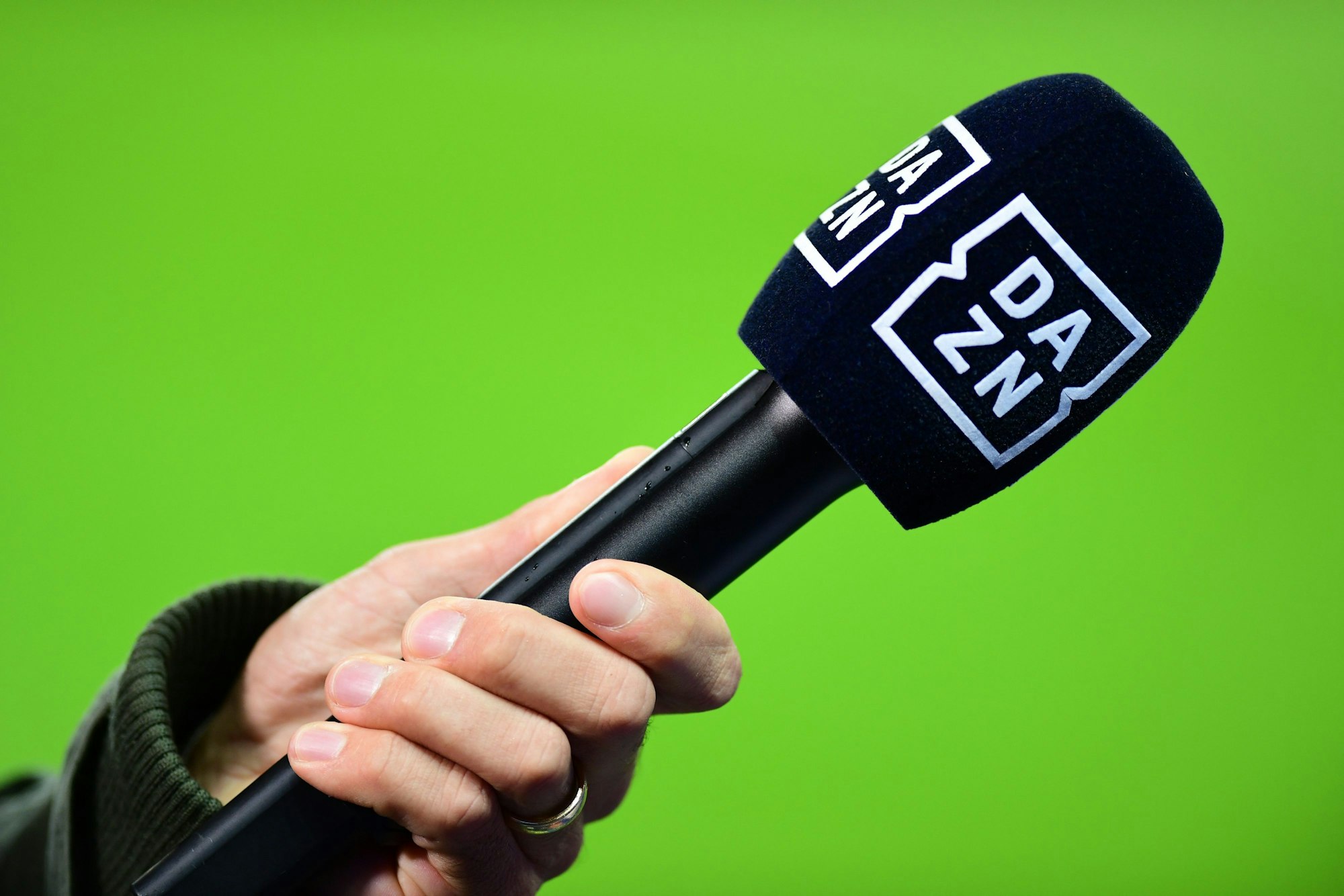Die Hand eines Reporters hält bei einem Interview vor dem Spiel ein Mikrofon mit der Aufschrift DAZN.
