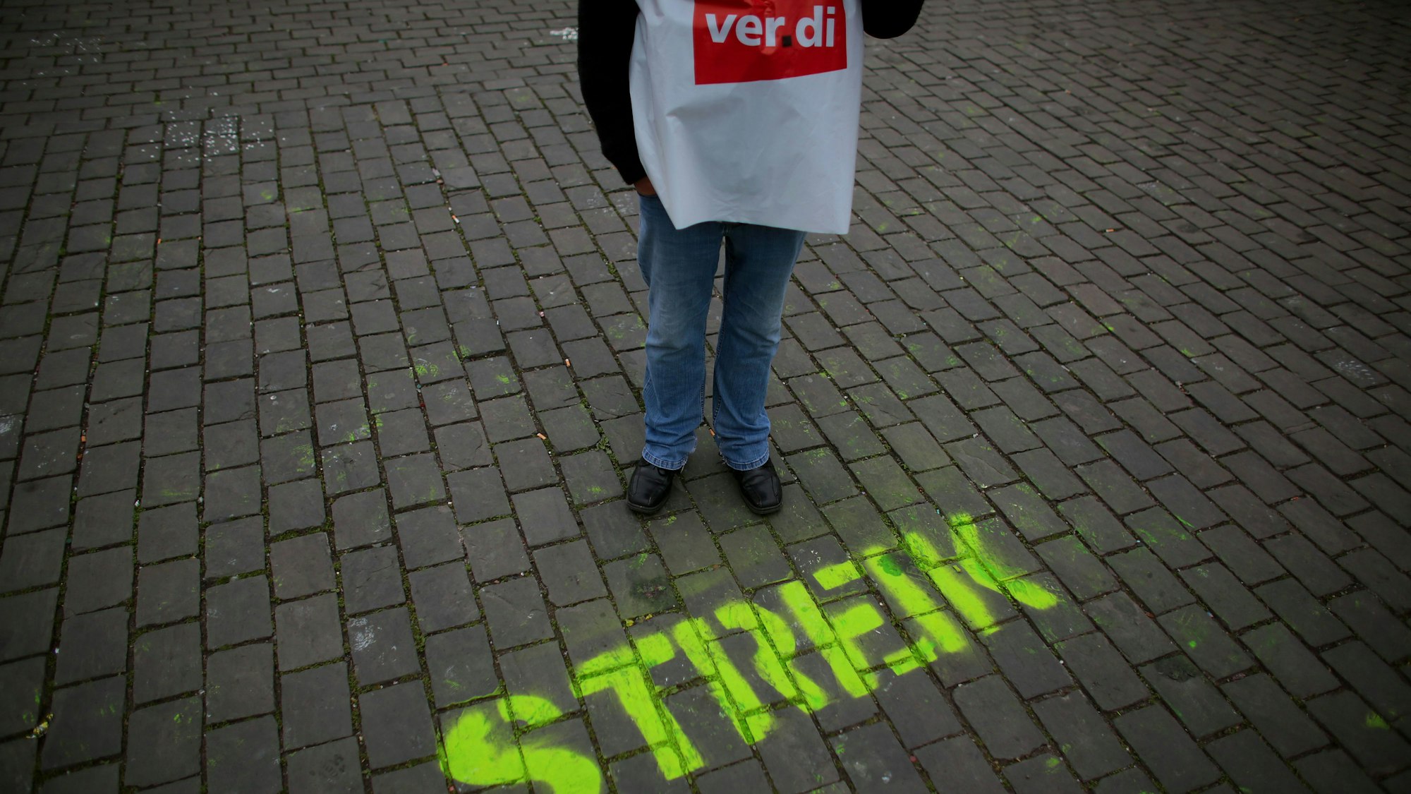 Ein Gewerkschafter steht neben dem auf die Straße gesprühten Wort „Streik“.