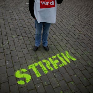 Ein Gewerkschafter steht neben dem auf die Straße gesprühten Wort „Streik“.
