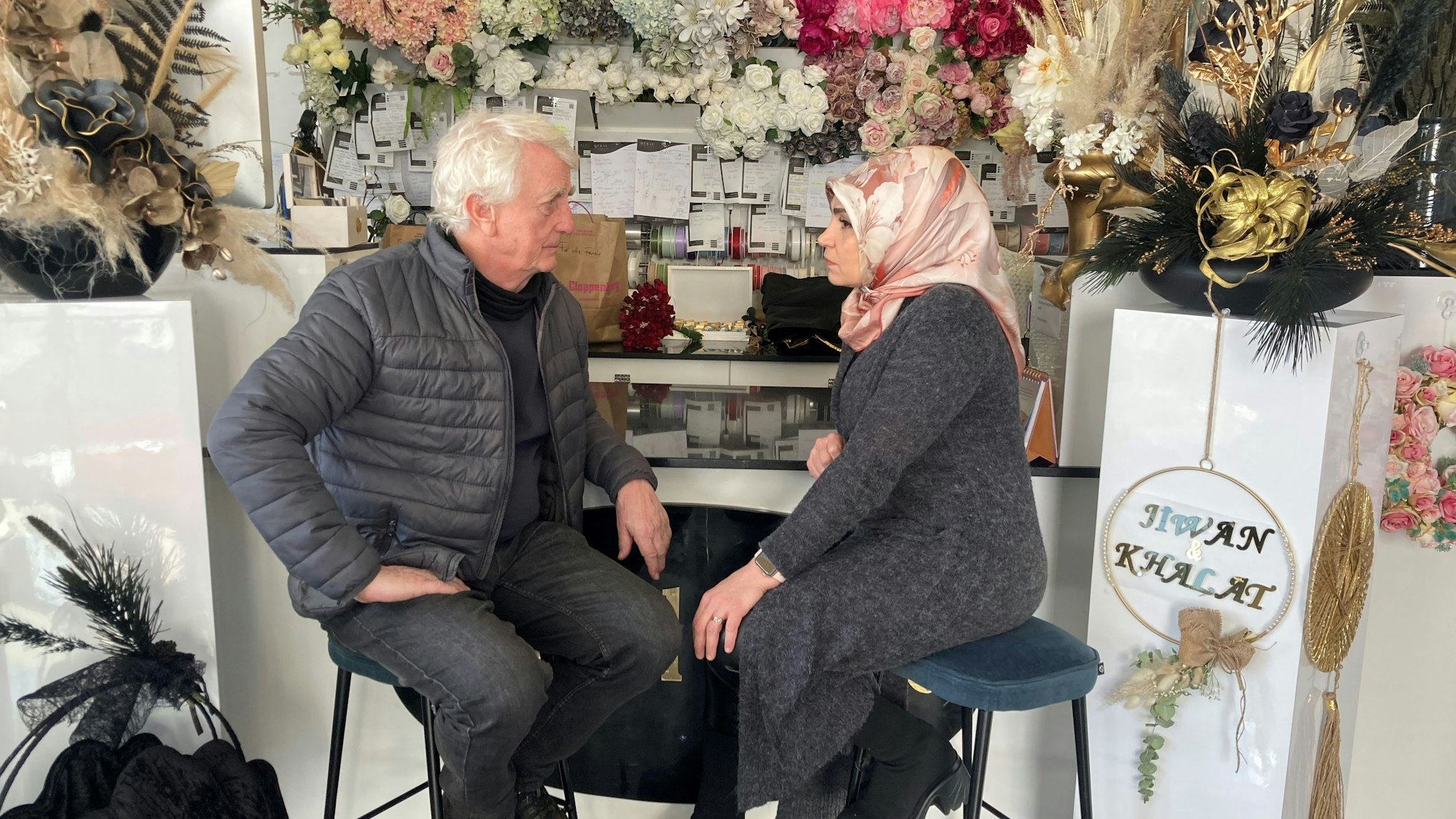 Peter Bach und Meral Sahin sitzen in ihrem Geschäft in der Keupstraße. Im Hintergrund sind Blumen zu sehen.