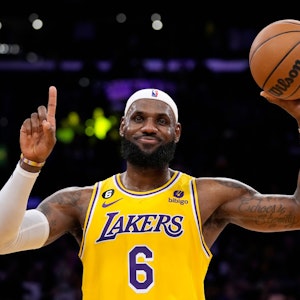 LeBron James lächelt zufrieden, zeigt mit dem Zeigefinger eine Eins und hält in der anderen Hand einen Basketball.