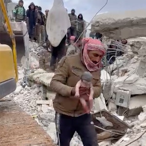 08.02.2023, Syrien, Jinderis: Ein Retter trägt ein neugeborenes Mädchen, nachdem er es aus Trümmern befreit hat.